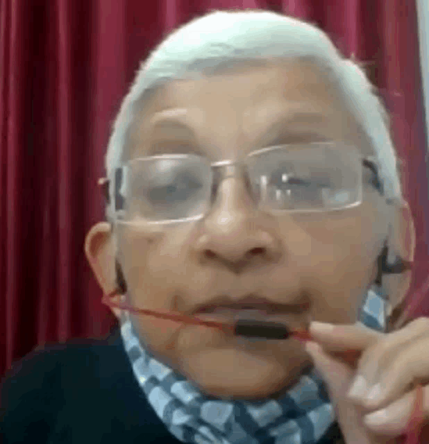 an elderly woman wearing glasses and a scarf is holding a pair of glasses in her mouth .