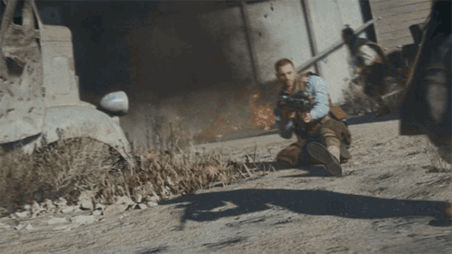 a man is kneeling down holding a gun in front of a burning building