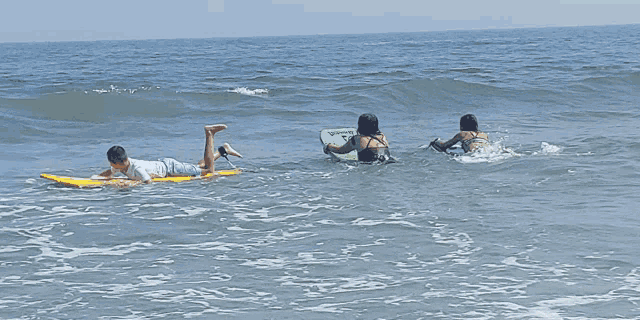 a person laying on a surfboard in the ocean while another person holds a green board