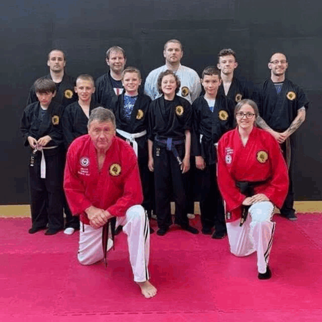 a group of people wearing martial arts uniforms are posing for a picture on a pink mat .