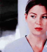 a close up of a woman 's face wearing a scrub top and looking at the camera .