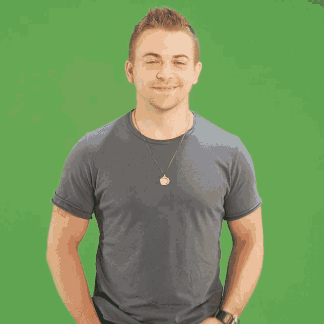 a man wearing a necklace and a watch stands in front of a green backdrop