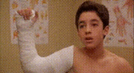 a young boy with a cast on his arm is flexing his arm .