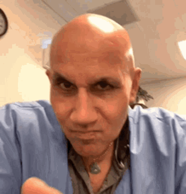 a bald man in a blue scrub is making a funny face while looking at the camera .