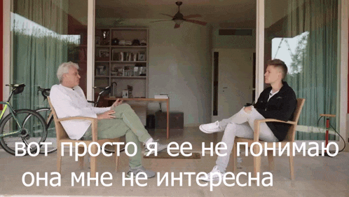 a man sits in a chair talking to another man in a room