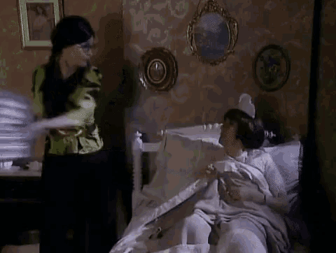 a woman is standing next to a woman in a bed .