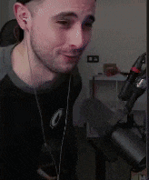 a man wearing headphones is standing in front of a microphone and smiling .