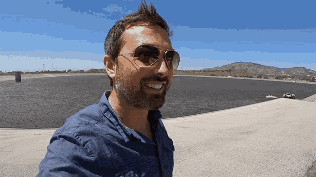 a man wearing sunglasses and a blue shirt is smiling