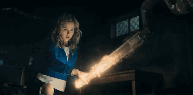 a girl in a blue jacket is holding a glowing object in her hands