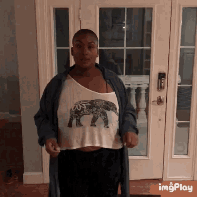 a woman wearing a crop top with an elephant on it is standing in front of a door that says imgplay