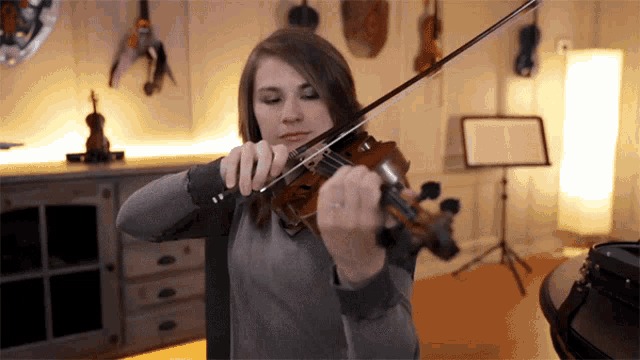 a woman playing a violin in a room with a music stand in the background