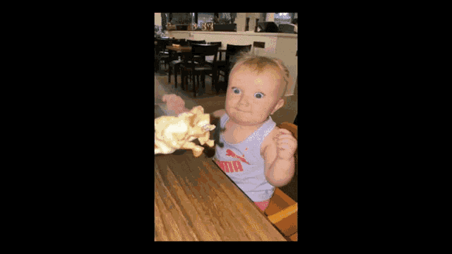a baby wearing a puma tank top is eating a piece of food