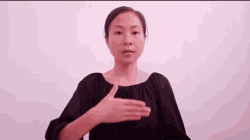 a woman is making a gesture with her hands while wearing a black shirt .
