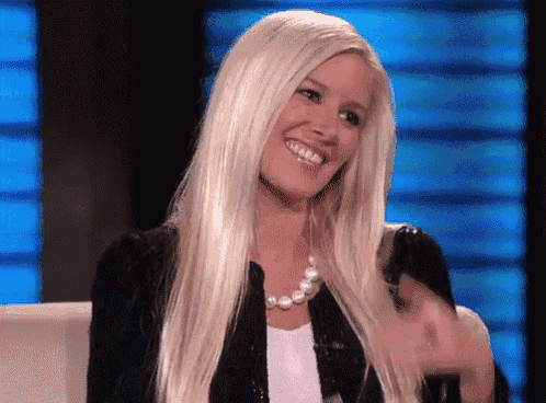 a woman with long blonde hair is smiling while wearing a black jacket and pearl necklace