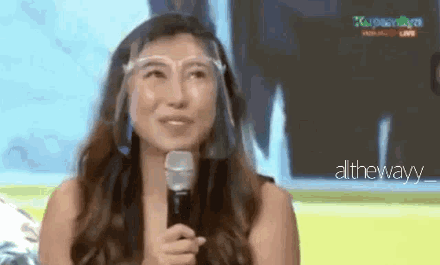 a woman wearing a face shield is holding a microphone .