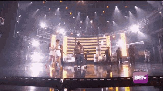a group of people are dancing on a stage in front of a bet sign