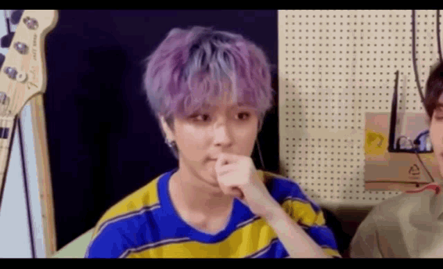 a young man with purple hair is sitting in front of a guitar in a recording studio .