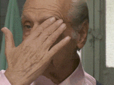 an older man in a pink shirt covers his face with his hand