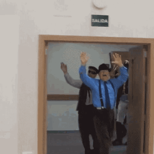 a man in a blue shirt and suspenders stands in front of a green exit sign