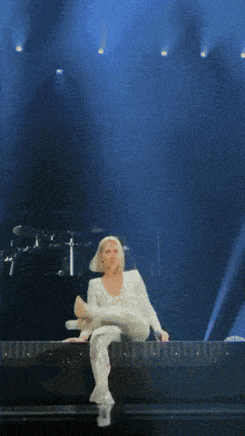 a woman in a white jumpsuit is sitting on a stage