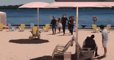 a group of people are dancing on a beach with a life preserver in the background