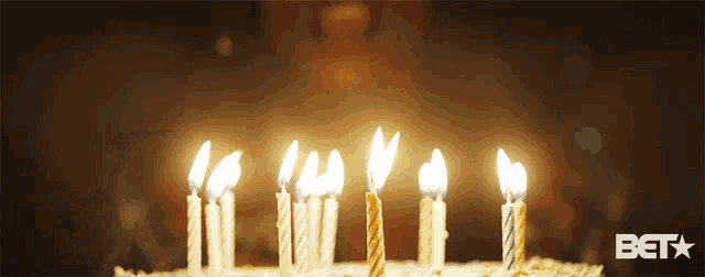 a birthday cake with candles lit up and a bet logo in the corner