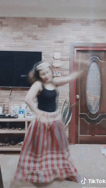 a woman in a plaid skirt is dancing in front of a tv and a door