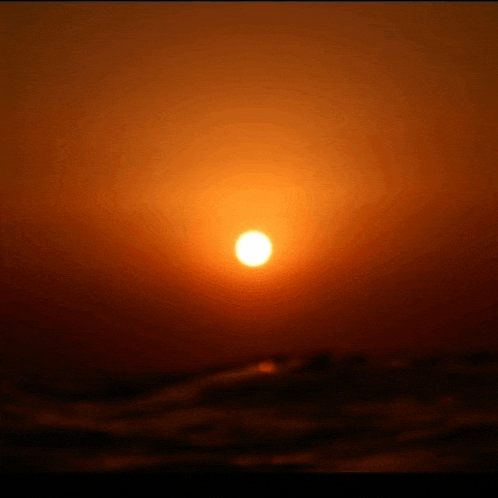 the sun is setting over the ocean and the waves are visible in the foreground .