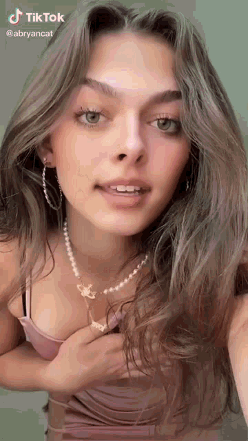 a woman is wearing a pearl necklace and earrings and taking a selfie .
