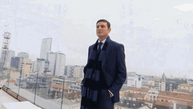 a man in a suit and scarf stands in front of a city skyline
