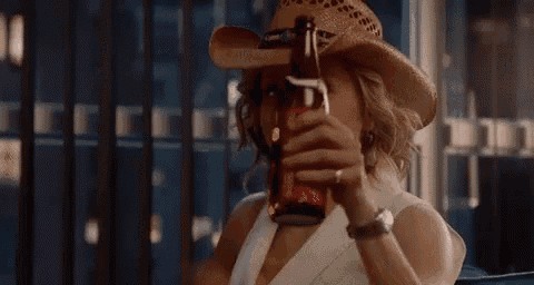 a woman in a cowboy hat is drinking from a bottle of beer .