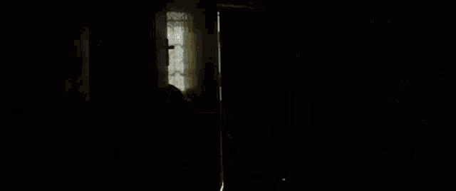 a man in a white shirt is standing in a doorway in a dark room holding a skateboard .