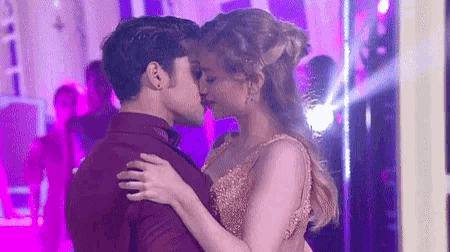 a man and a woman are kissing while dancing in a room with purple lights .
