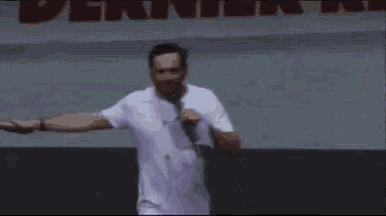 a man in a white t-shirt is dancing with his arms outstretched and a microphone in his hand .