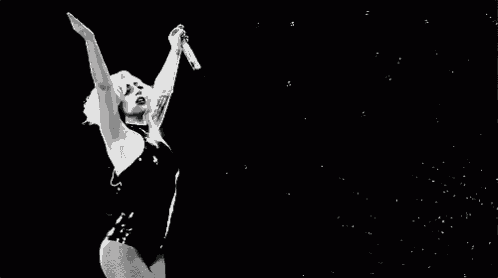 a black and white photo of a woman in a swimsuit singing into a microphone with her arms in the air .