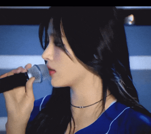 a woman in a blue shirt is singing into a black microphone
