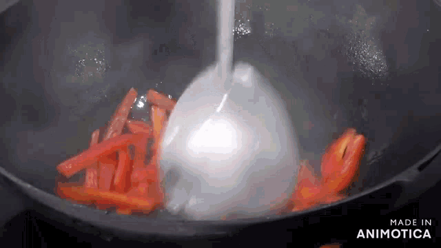 carrots are being cooked in a wok with a ladle