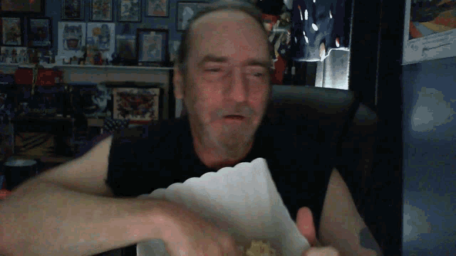 a man in a black shirt is eating popcorn from a white box