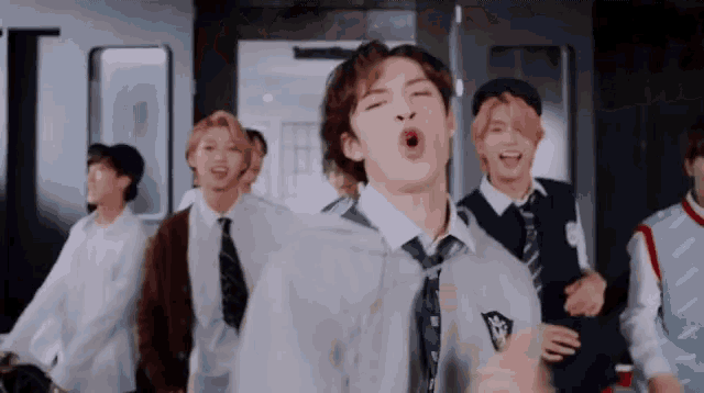 a group of young men in school uniforms and ties are dancing together in a room .
