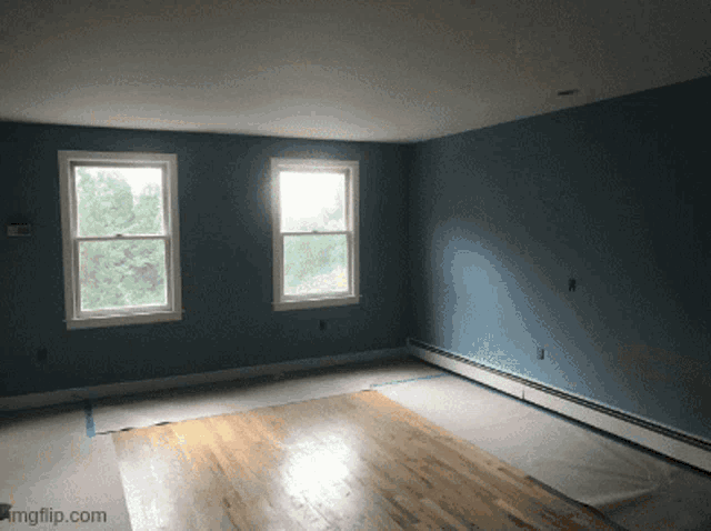 an empty room with blue walls and hardwood floors with a watermark that says imgflip.com