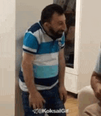 a man with a beard wearing a blue and white striped shirt is standing next to a couch .