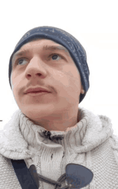 a man wearing a hat and a sweater looks up