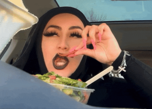 a woman wearing a black hijab is eating a salad in a car