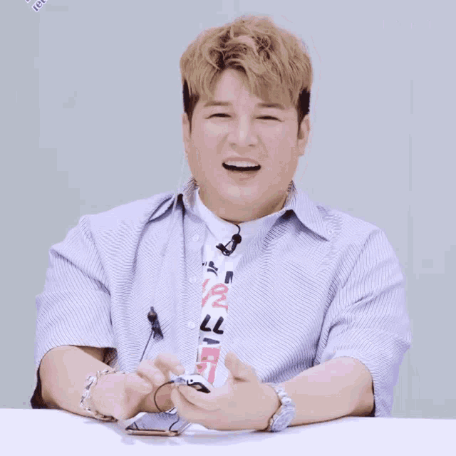 a man wearing a striped shirt and tie is smiling and holding a cell phone