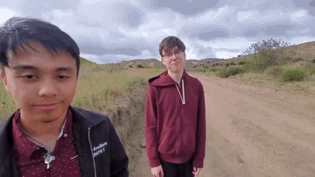 two young men are standing next to each other on a dirt road in a field