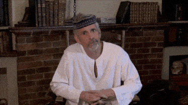 a man wearing a white shirt and a blue hat is sitting in front of a bookshelf