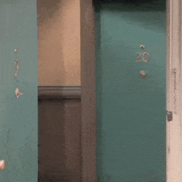 a man is standing in front of a green door with the number 20 written on it .