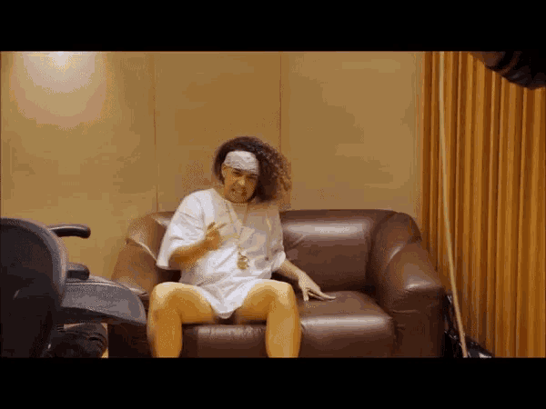 a man with curly hair is sitting on a couch wearing a headband and giving a thumbs up