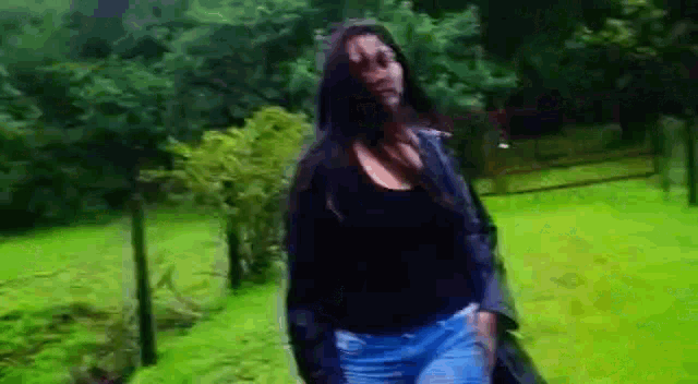 a woman in a black top and blue jeans is standing in a field of grass .