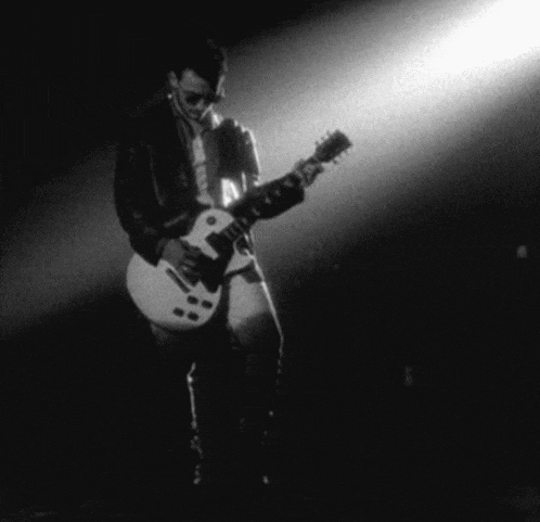 a man is playing a white guitar in a dark room